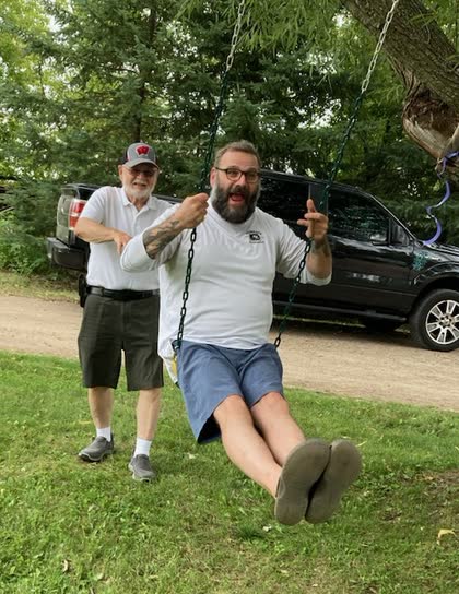 Scott on a tree swing while his dad George watches