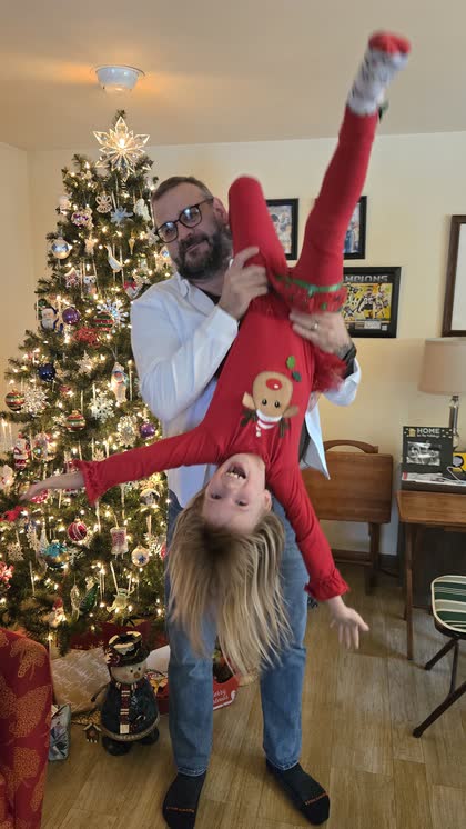 Scott holding his granddaughter Octavia upside down by a Christmas tree