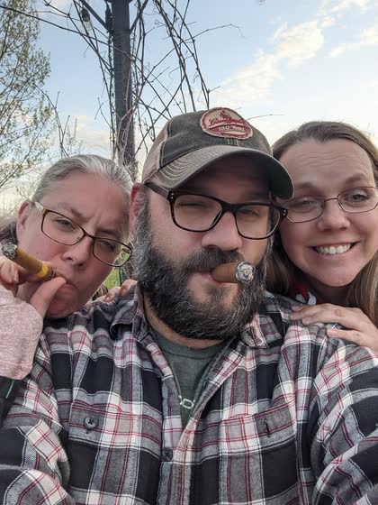 Scott with a cigar between his teeth, posing with Robin and Tami outdoors