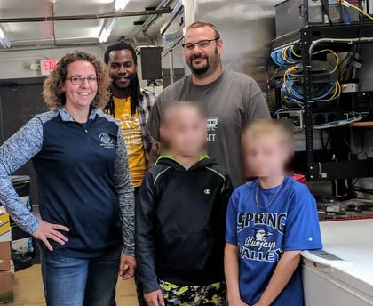Scott with Boys and Girls Club staff and two children, standing in front of a network equipment rack; the children's faces are blurred