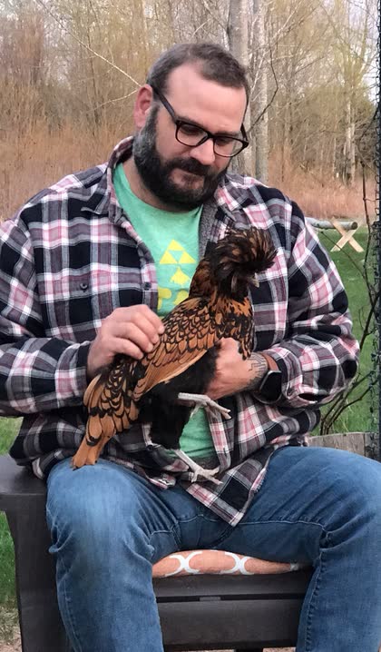 Scott sitting in a chair holding a brown and black chicken