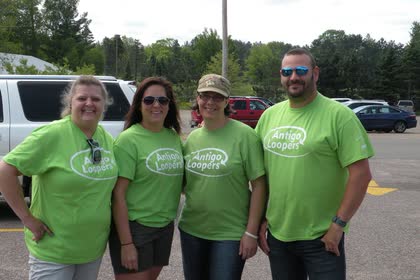 Four people in matching green Antigo Loopers shirts posing in a parking lot