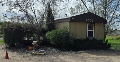 The outside of the small tan office building with the number 1007 on it, surrounded by trees and shrubs